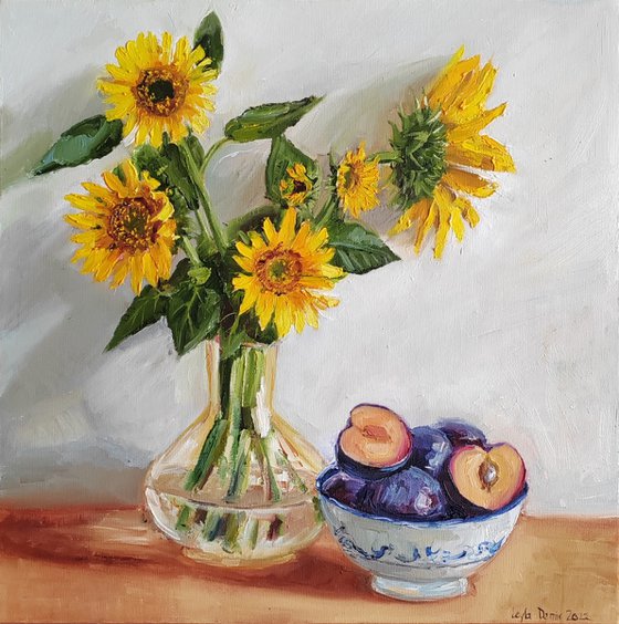 . Yellow sunflower bouquet in glass vase with plums in a porcelain bowl still life