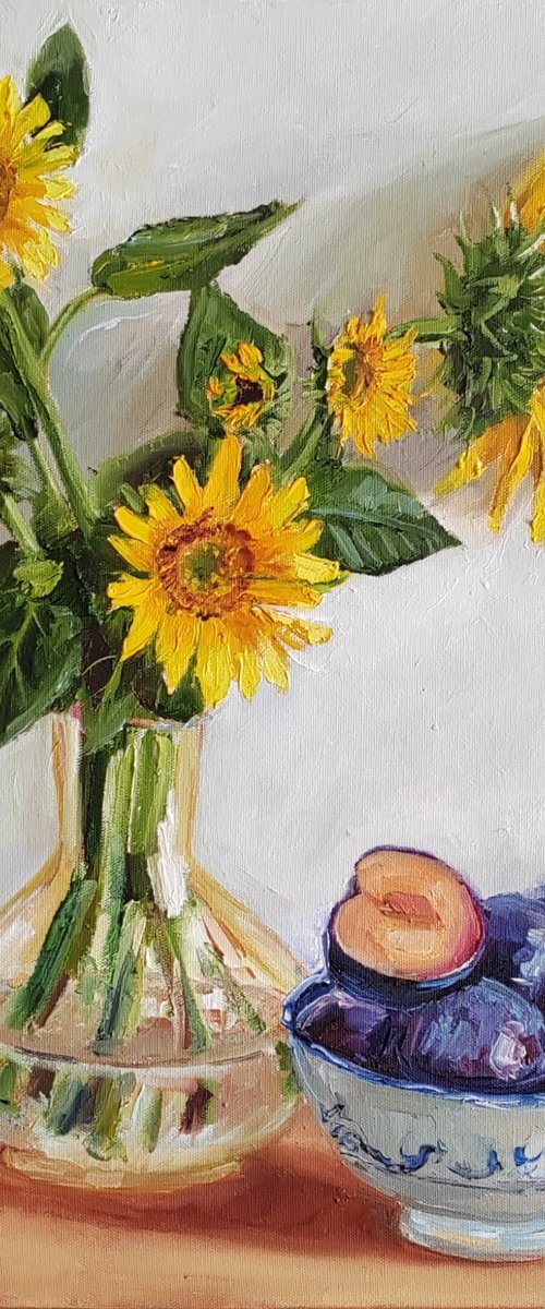 . Yellow sunflower bouquet in glass vase with plums in a porcelain bowl still life by Leyla Demir
