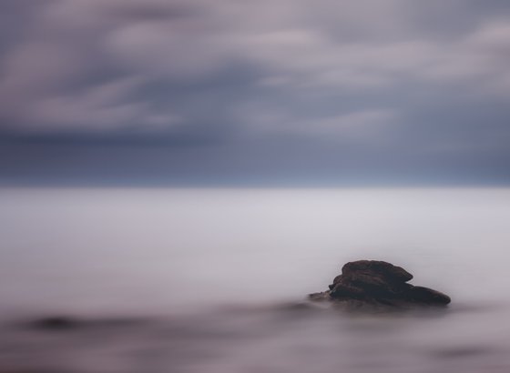 A lone rock in the silky sea