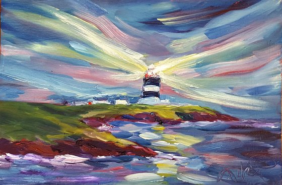 The light of Hook Head Lighthouse illuminates the sky at Dusk