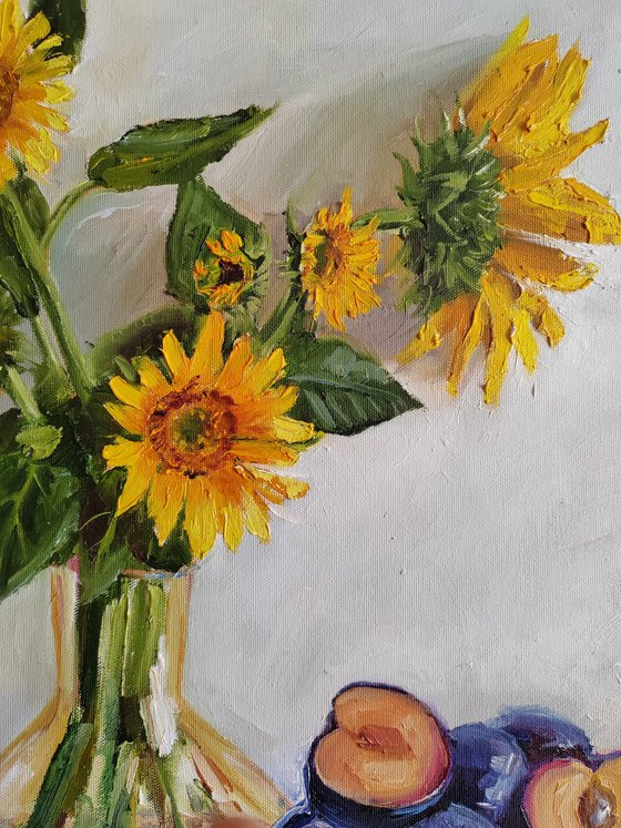. Yellow sunflower bouquet in glass vase with plums in a porcelain bowl still life