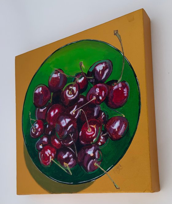 Cherries in a green glass bowl against a gold background