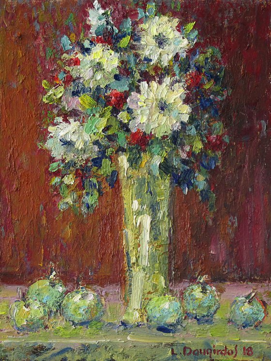 The flowers in the vase with apples.